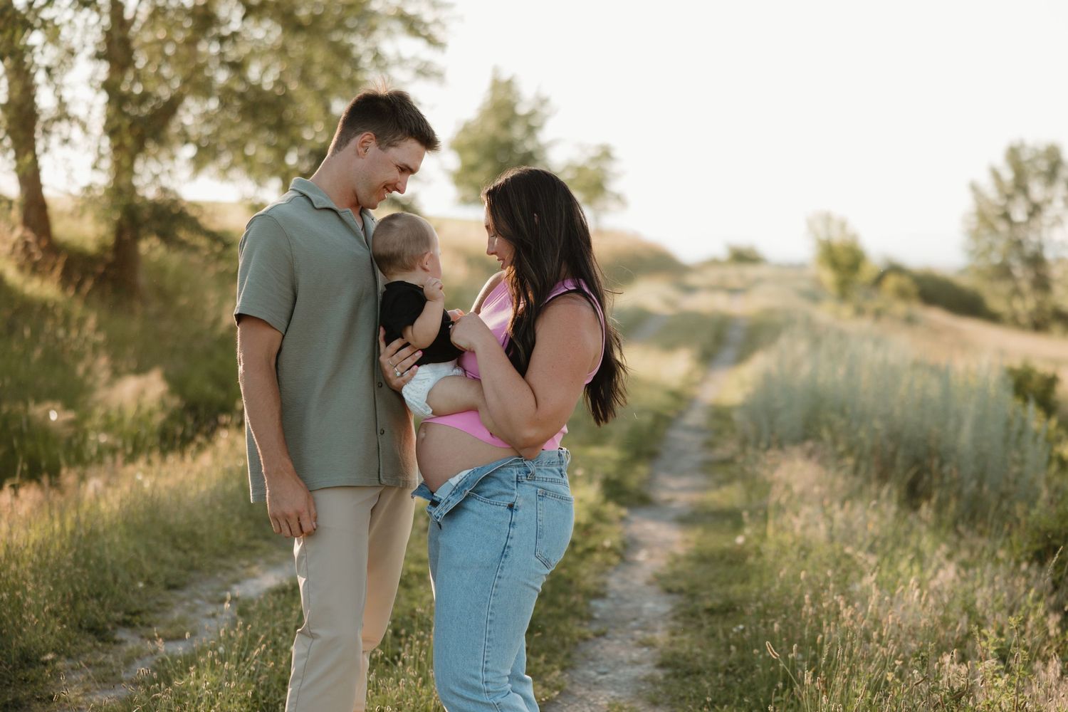A couple shares a romantic moment together on a grassy hillside path during golden hour sunset.