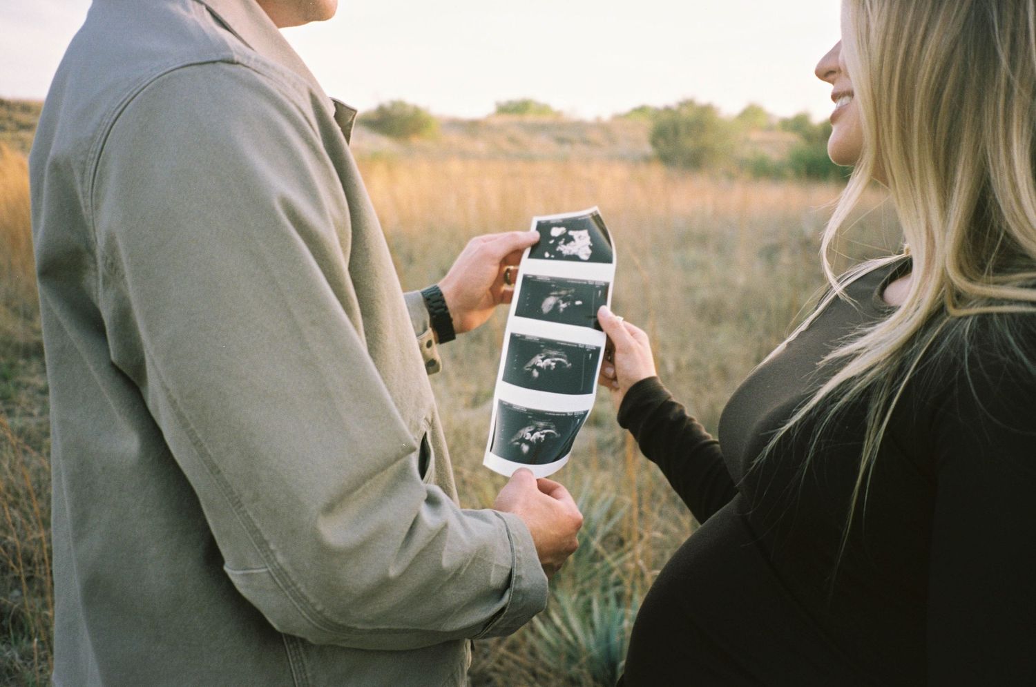 Expecting couple holding ultrasound photos together in a golden field during a maternity announcement shoot.