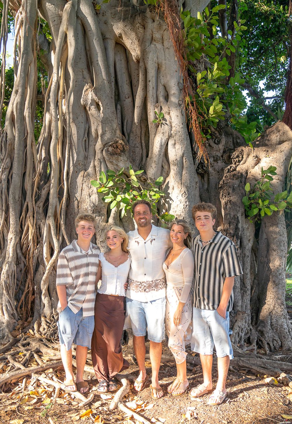 A group of people standing together in front of a large banyan tree with hanging aerial roots in a tropical setting.
