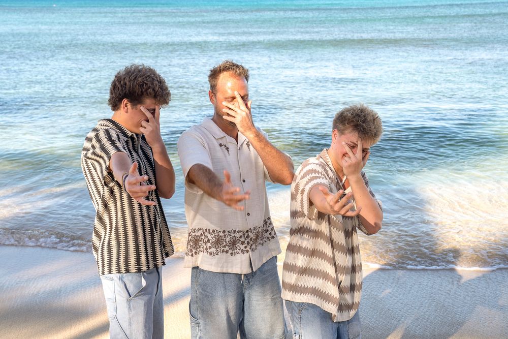 Group of friends laughing and enjoying a sunny day at the beach with ocean waves in the background.