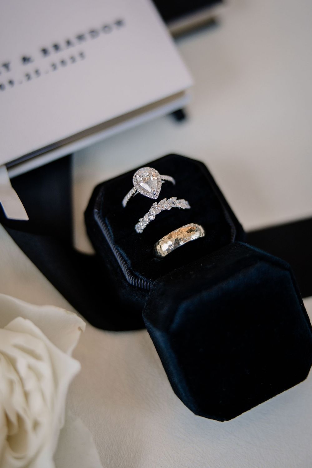 Pear-shaped diamond engagement ring and wedding bands displayed in black velvet ring box.