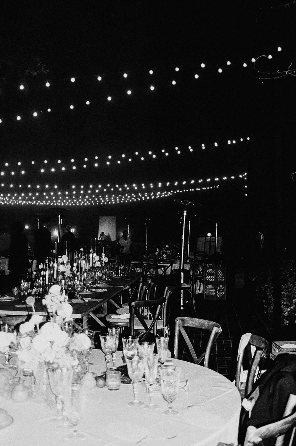 String lights create a magical ambiance at an outdoor evening reception with tables set for dining.