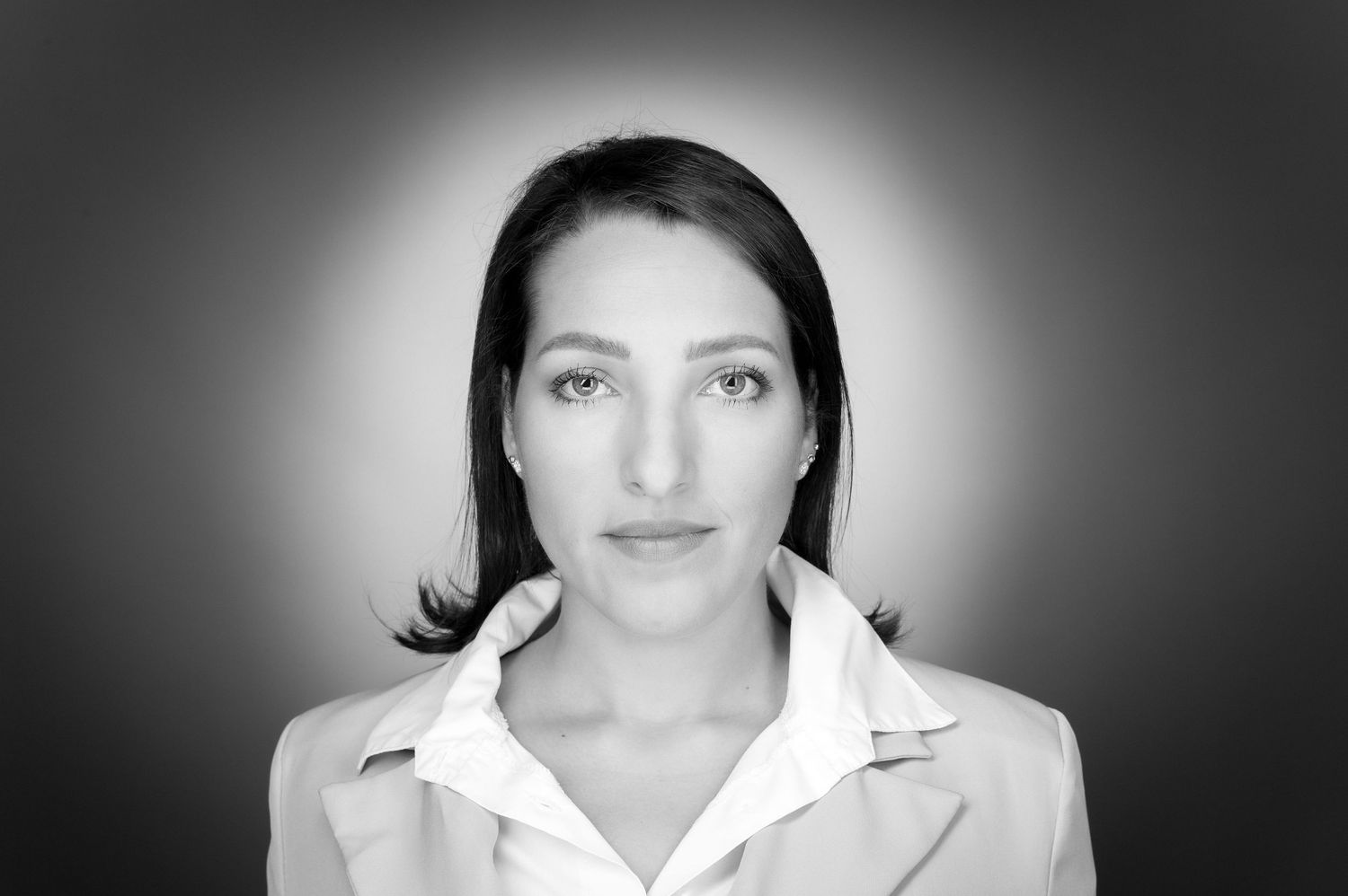 Black and white portrait of a person wearing a white collared shirt against a dark background.