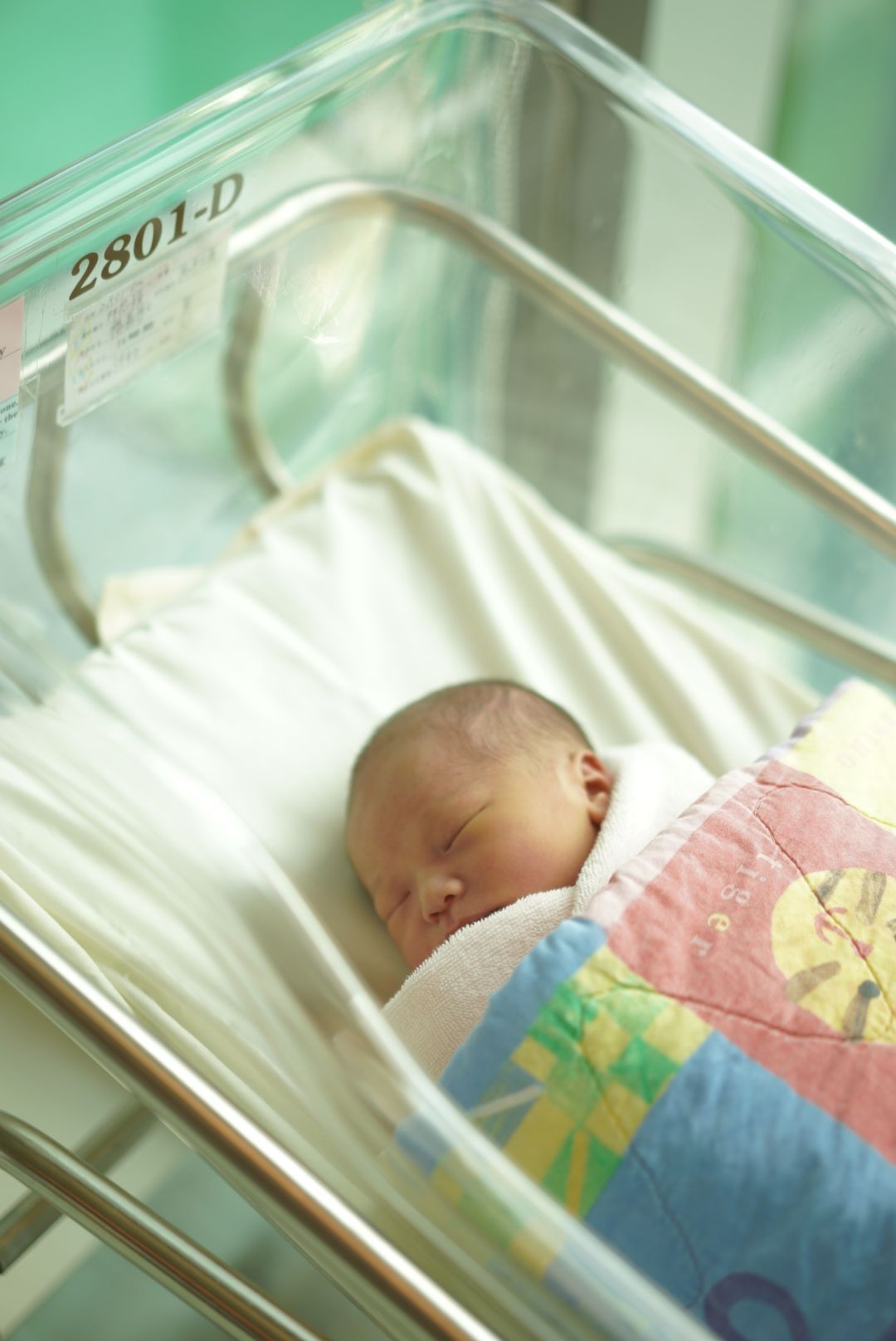 A newborn baby rests peacefully in a hospital bassinet with colorful blankets一個新生兒安詳地躺在醫院的嬰兒床裡，床上蓋著色彩鮮豔的毯子。