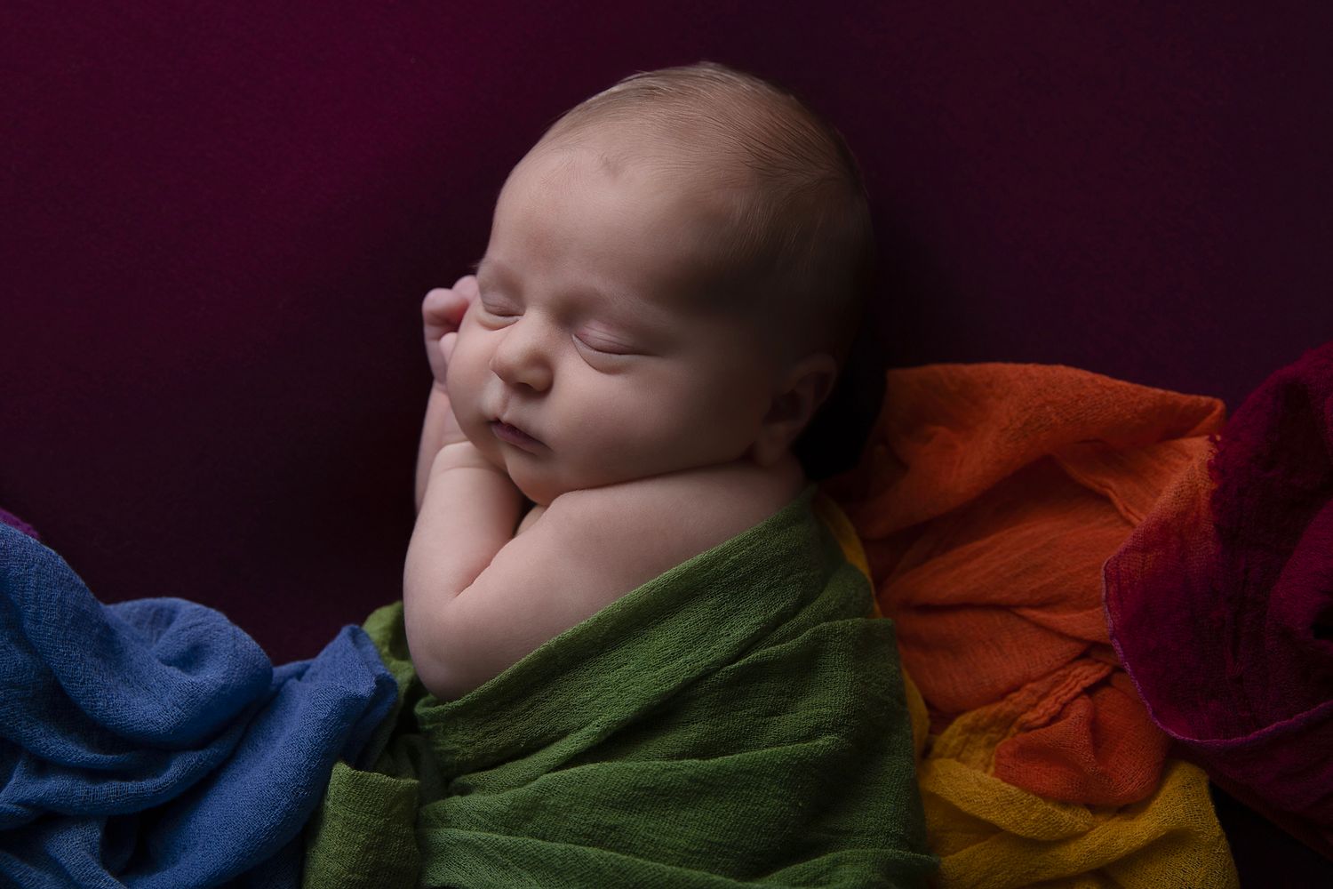 Baby sleeping peacefully on colorful fabric in artistic newborn photography series.
