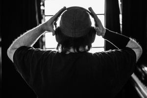 Black and white photo of a man seen from behind wearing headphones and a beanie hat.