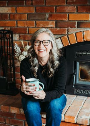 A person in black sits on brick steps holding a turquoise coffee mug against a rustic red brick wall background.
