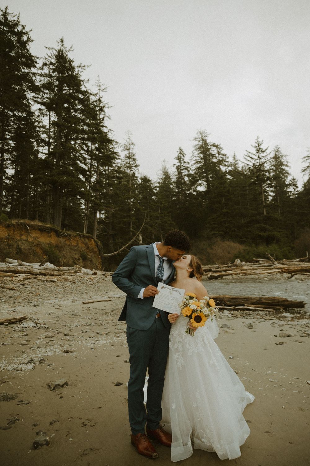 A romantic beach wedding scene with evergreen trees and driftwood along a Pacific Northwest shoreline.