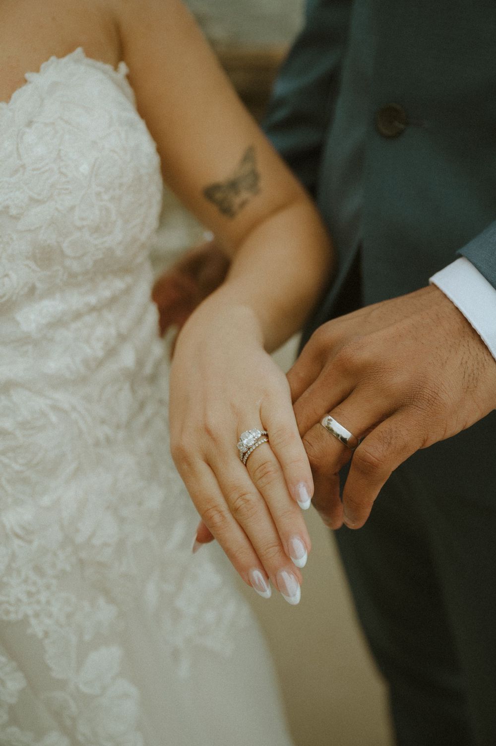 Close-up of wedding rings and hands showing the newlyweds' jewelry against white dress fabric.