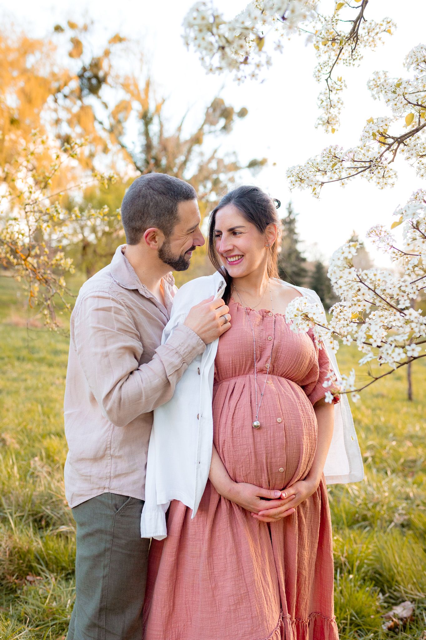 Future maman et papa partageant un moment tendre sous les cerisiers en fleurs