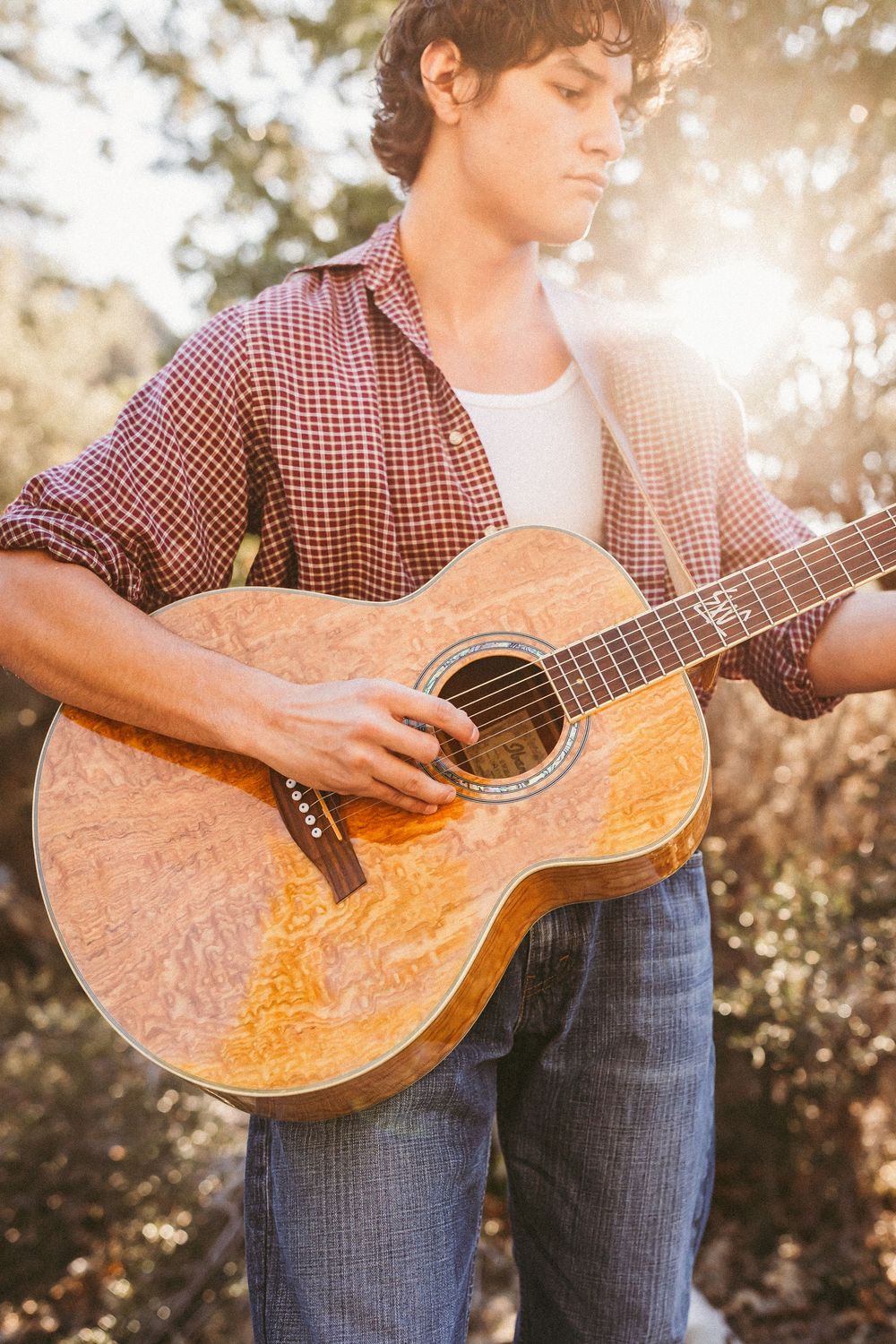 Sunlit close-up shots of acoustic guitar being played in casual outdoor setting with denim jeans and plaid shirt.