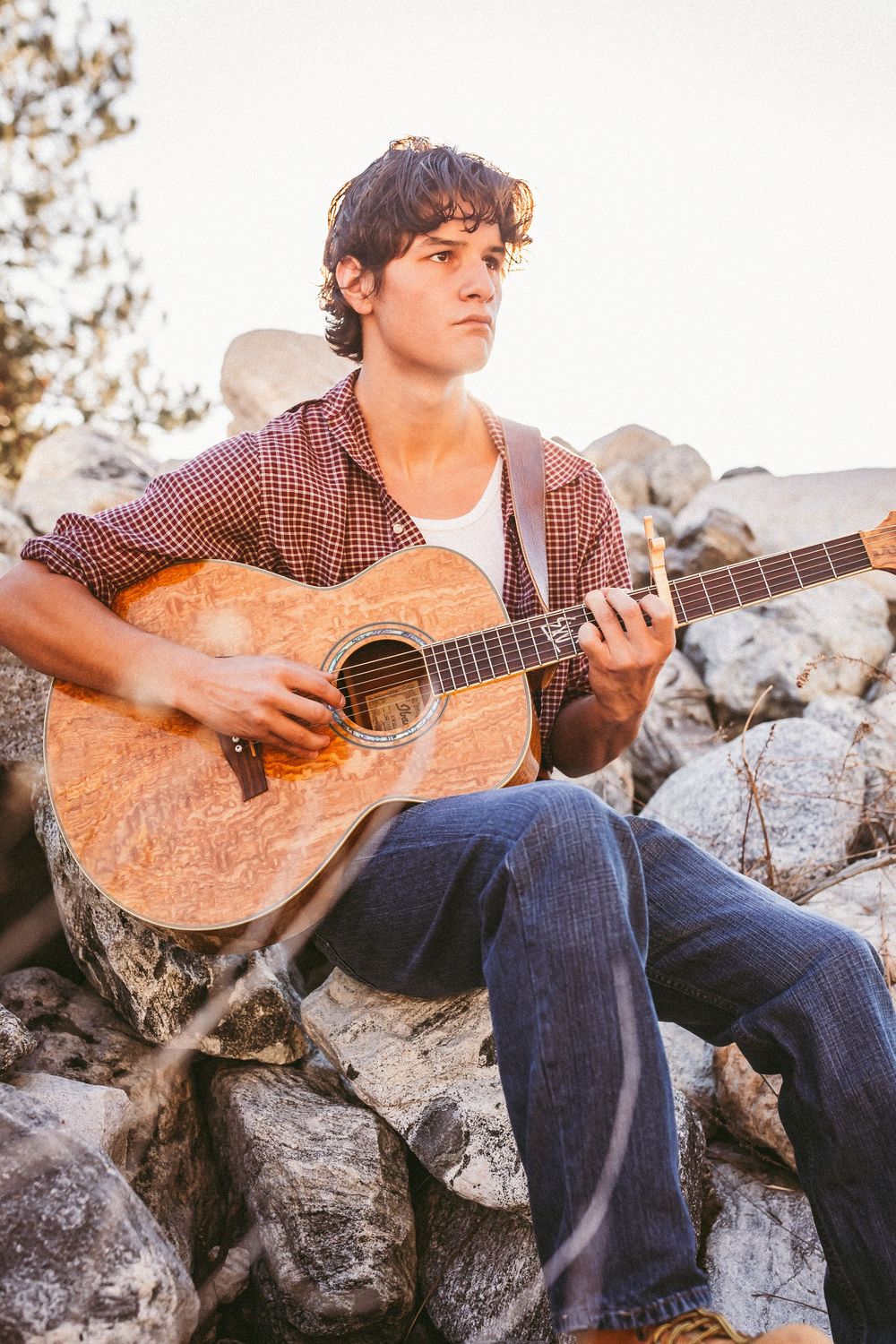 A musician plays acoustic guitar while sitting on rocky terrain during golden hour.