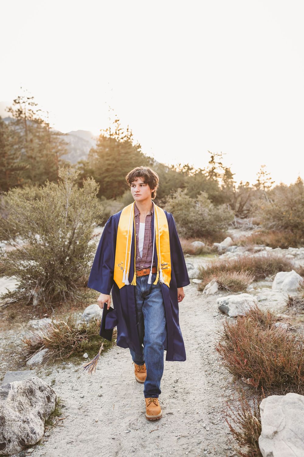 A person wearing a navy and yellow varsity jacket walks along a desert trail during golden hour sunset.