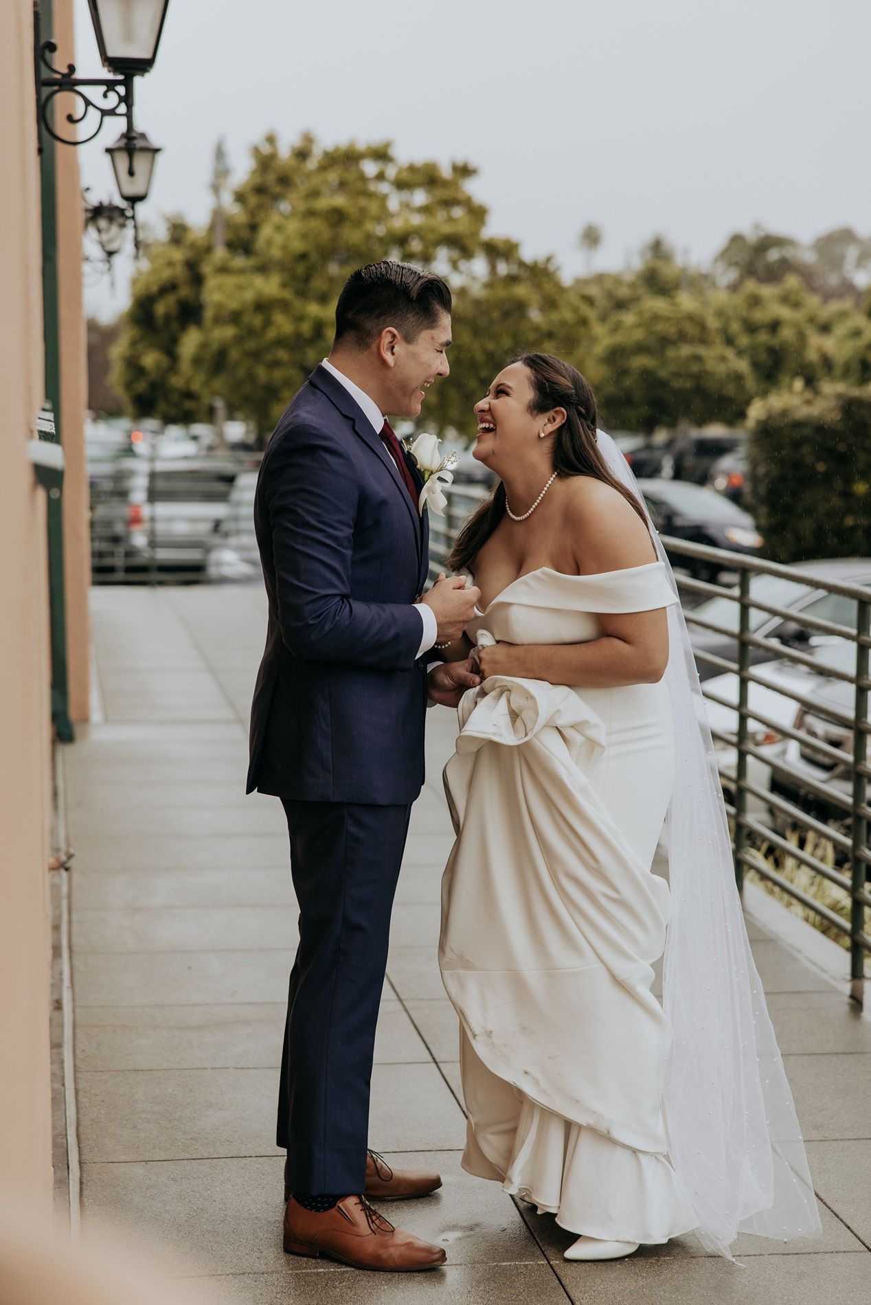 A joyful moment between a bride in white dress and groom in navy suit dancing on a covered outdoor patio at BRICK Liberty Station.