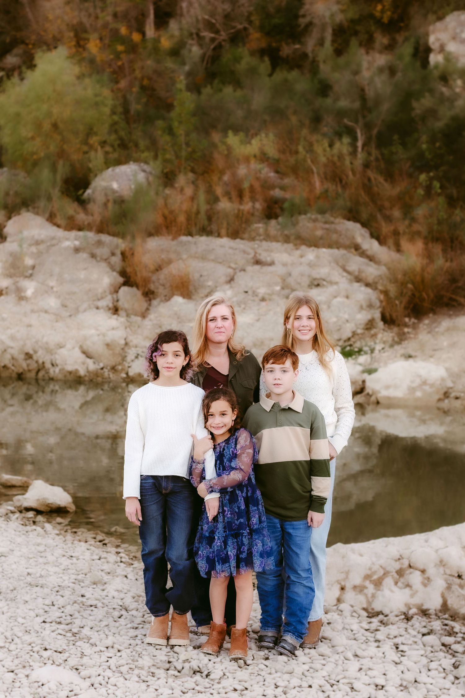 A group of people sit together on white rocks by a creek bed surrounded by autumn trees and foliage.