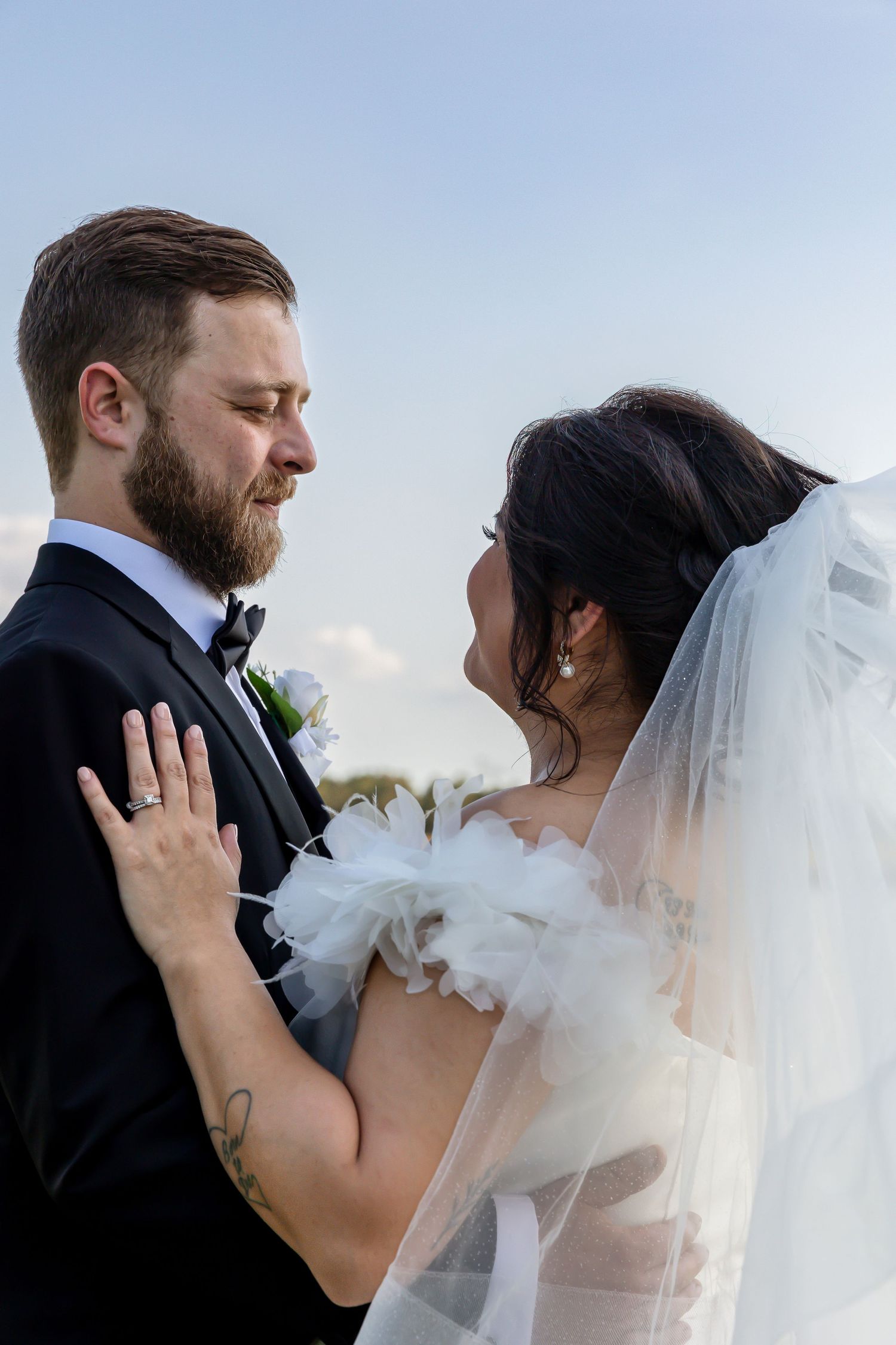 A romantic wedding couple embraces under a flowing white veil during their outdoor ceremony.