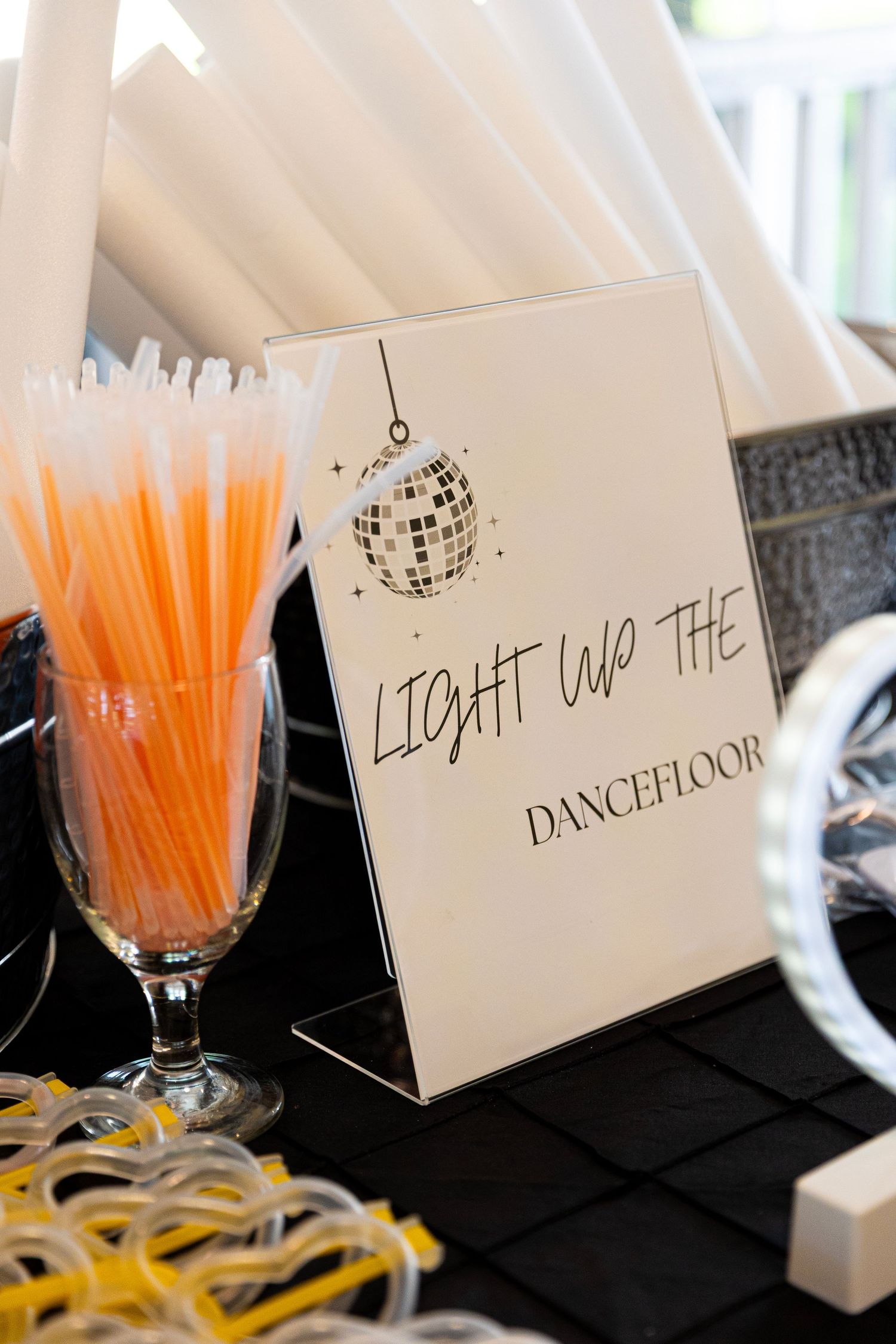 Orange glow sticks and white tent cards displayed on black tablecloth at wedding reception.