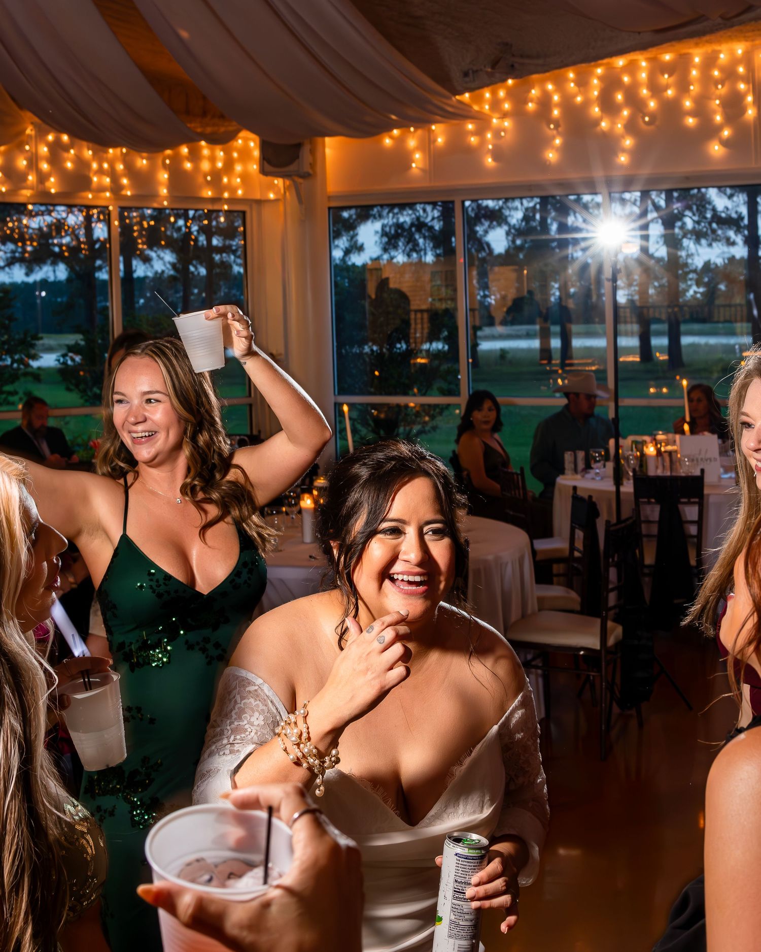 Wedding guests dance and celebrate under warm string lights at an evening reception venue.