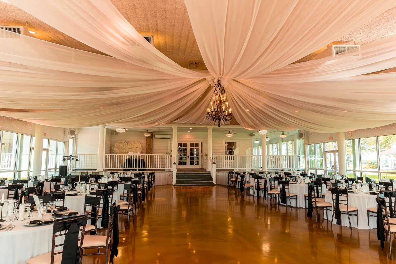 Elegant wedding reception venue with draped fabric ceiling, black chairs and round tables set for a formal celebration.