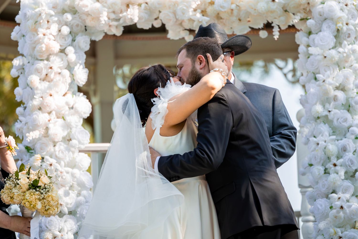 Romantic wedding couple sharing a kiss under an elegant arch decorated with cascading white orchids and flowers.