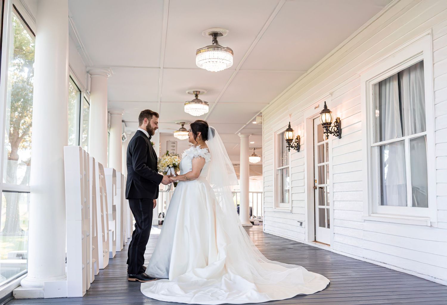 A wedding couple shares romantic moments in a bright white hallway with elegant lighting fixtures.