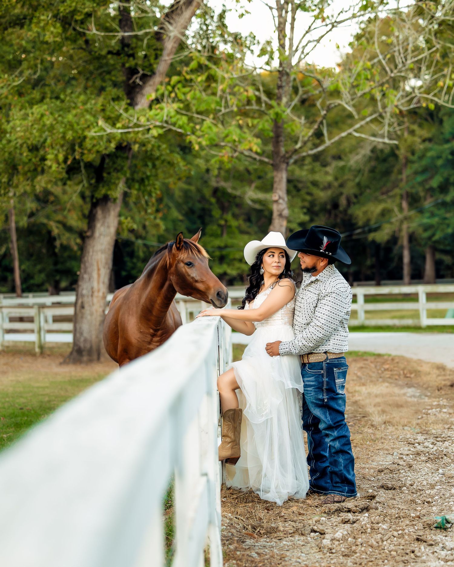 A romantic engagement photoshoot with a couple and their horse in a rustic outdoor setting with white fencing.