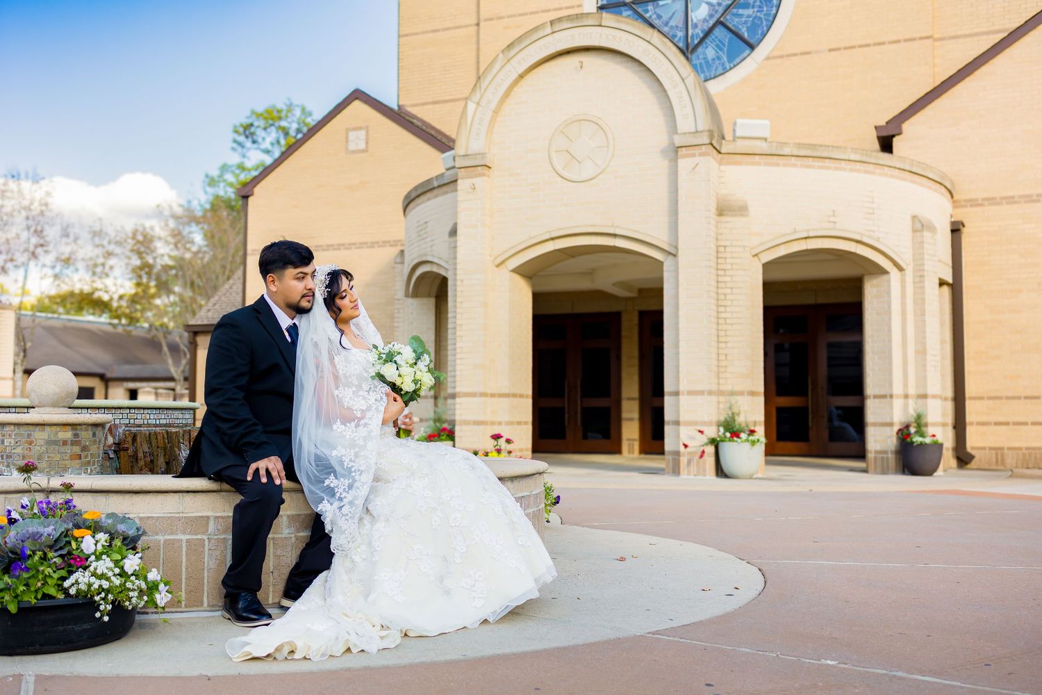 A bride and groom share a romantic moment outside a beige stone church building with arched windows and columns.
