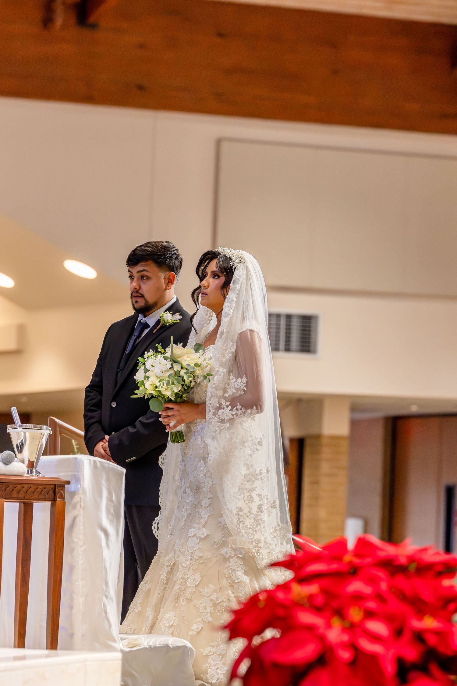 A wedding ceremony in a church with red poinsettias decorating the aisle during a winter celebration.