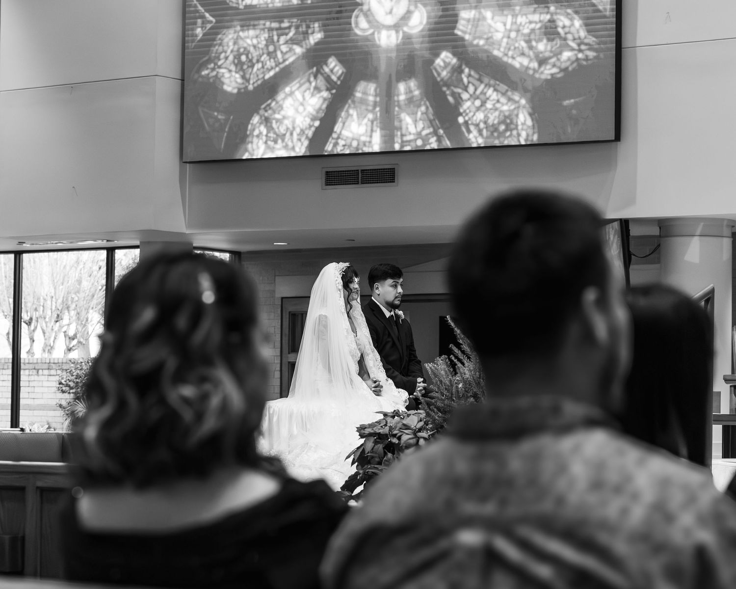 A black and white photograph shows a group of people sitting in a row at what appears to be an indoor event.
