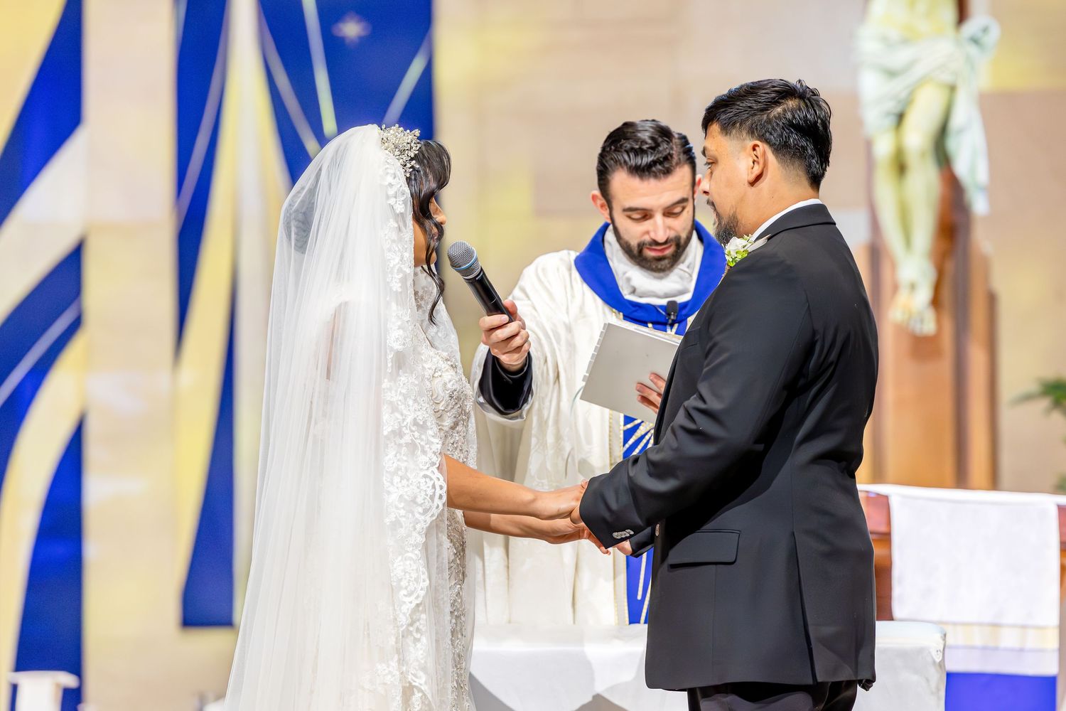 Wedding ceremony in a church with blue and white decor as couple exchanges vows at the altar.