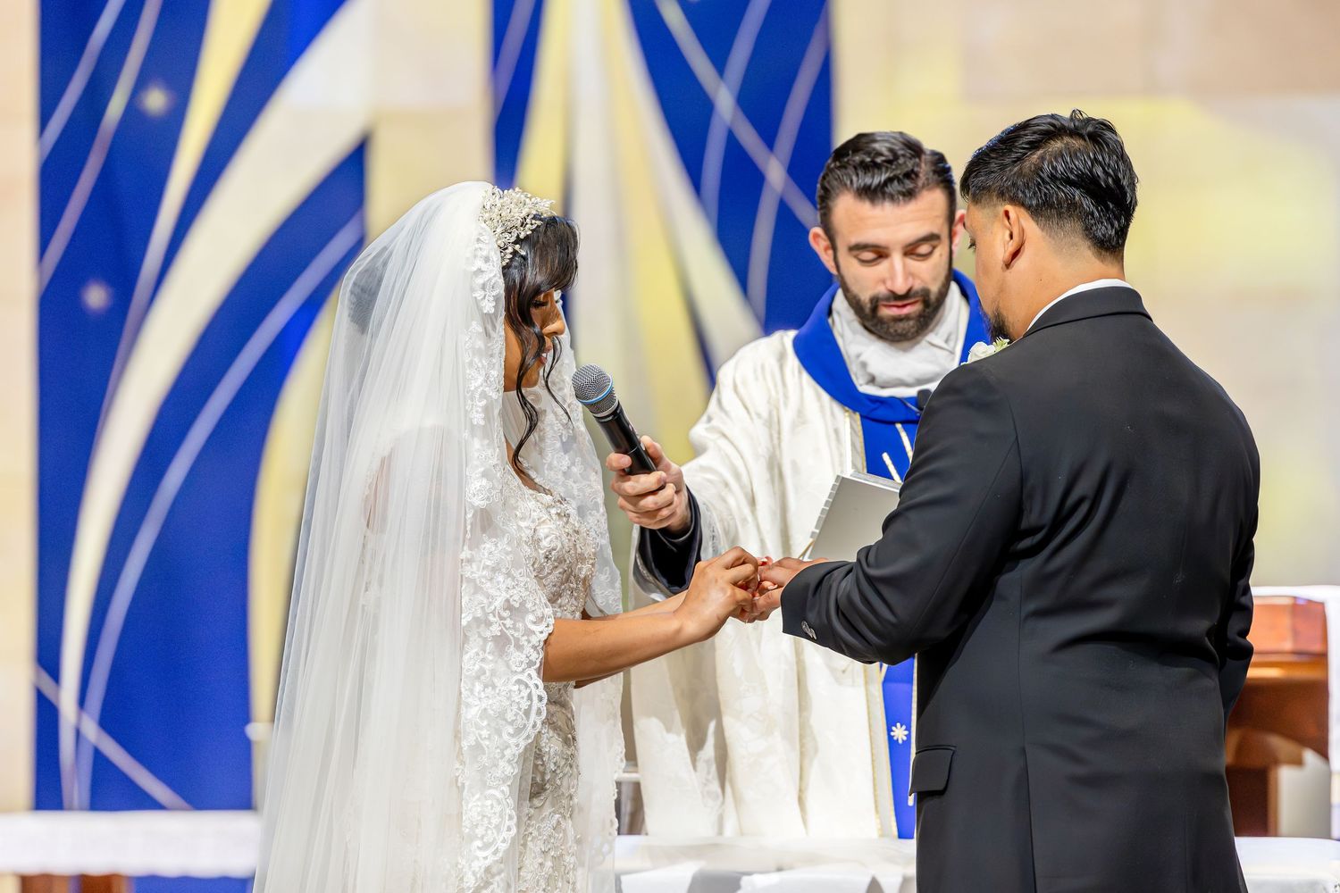 A solemn wedding ceremony moment with blue stained glass windows visible in the church.
