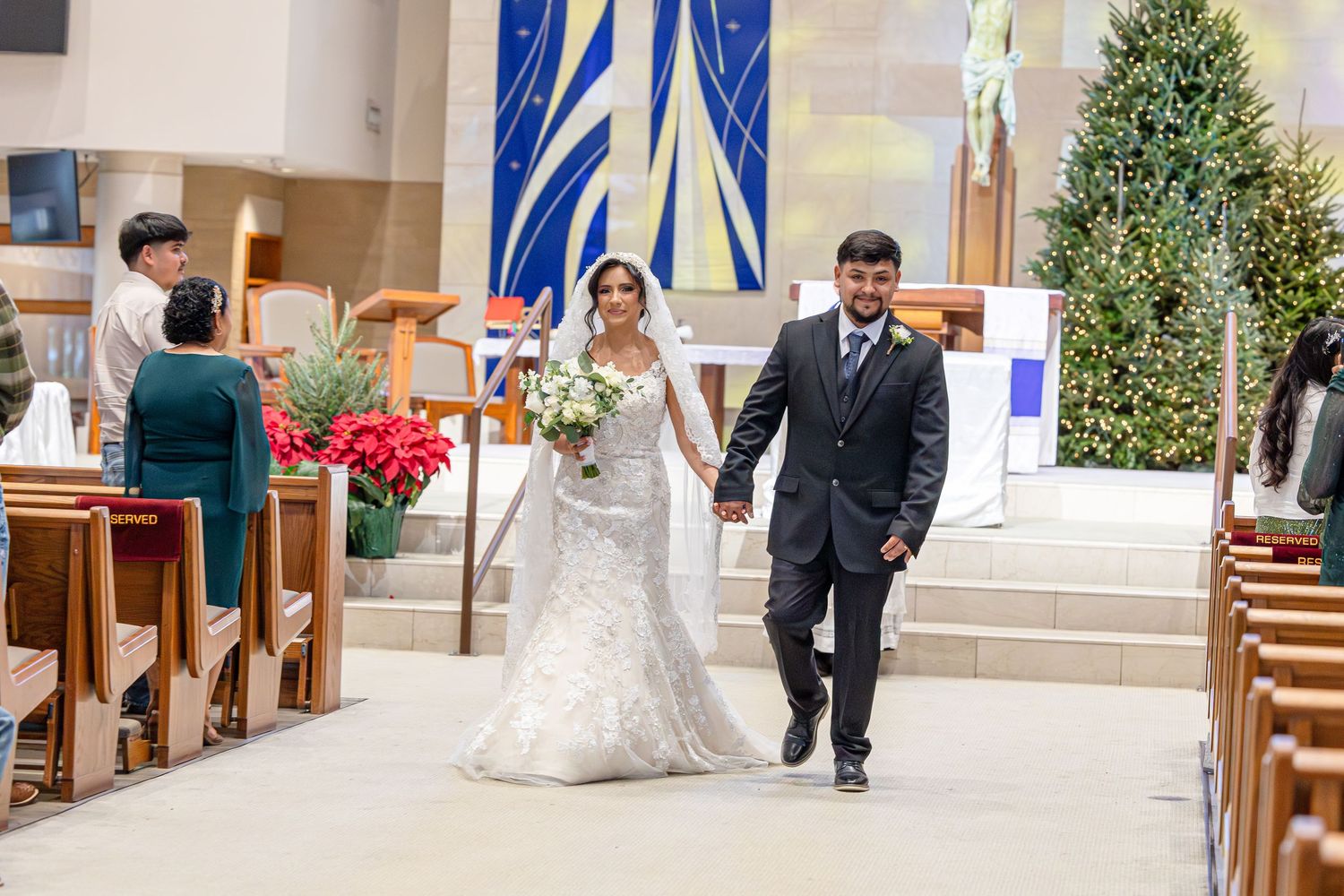 A couple shares a romantic moment during their wedding ceremony in a church decorated with blue banners and greenery.