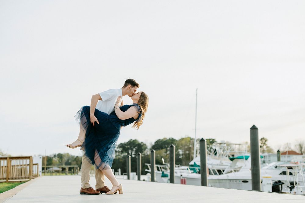 A couple dances and embraces on a beach boardwalk during a romantic photoshoot at sunset.