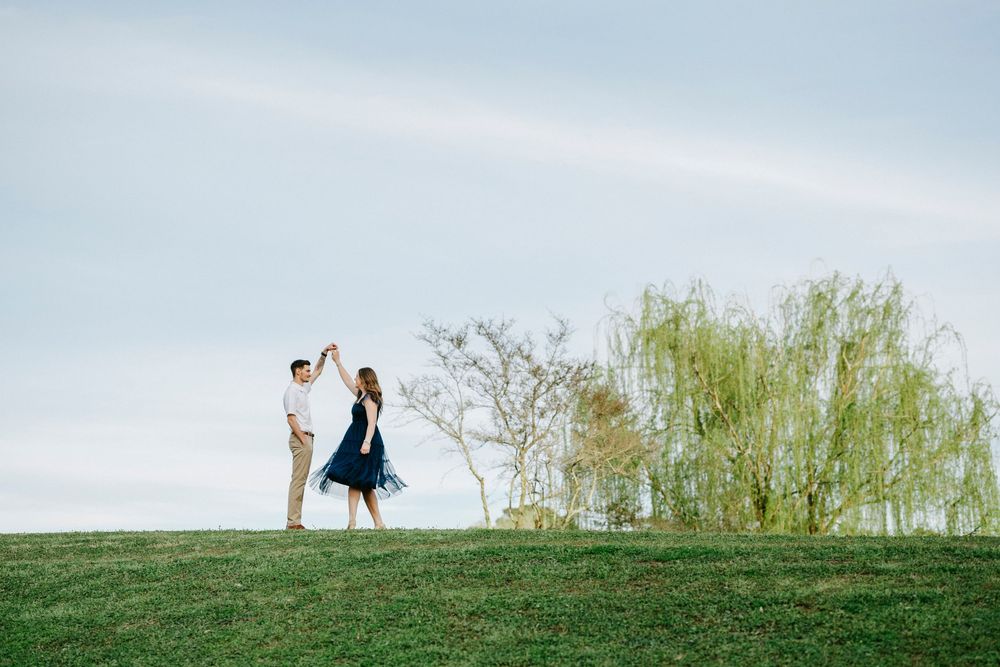 A couple poses together in a romantic outdoor setting with green grass and trees in the background.