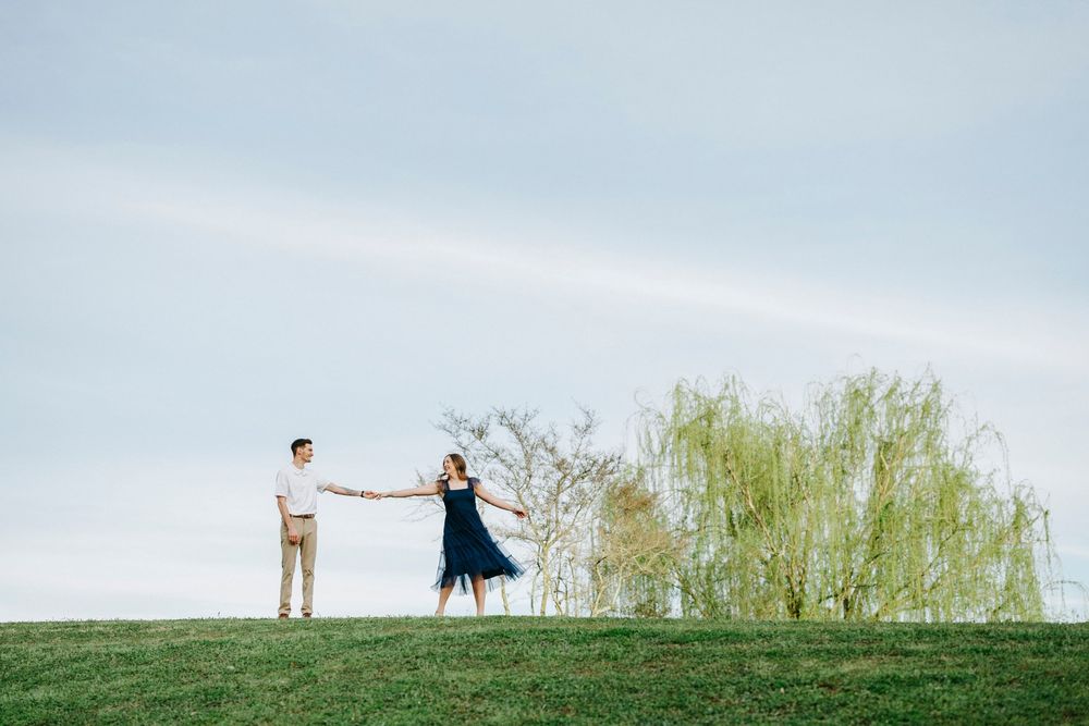 A panoramic view shows two people walking along a grassy hilltop against a cloudy sky.