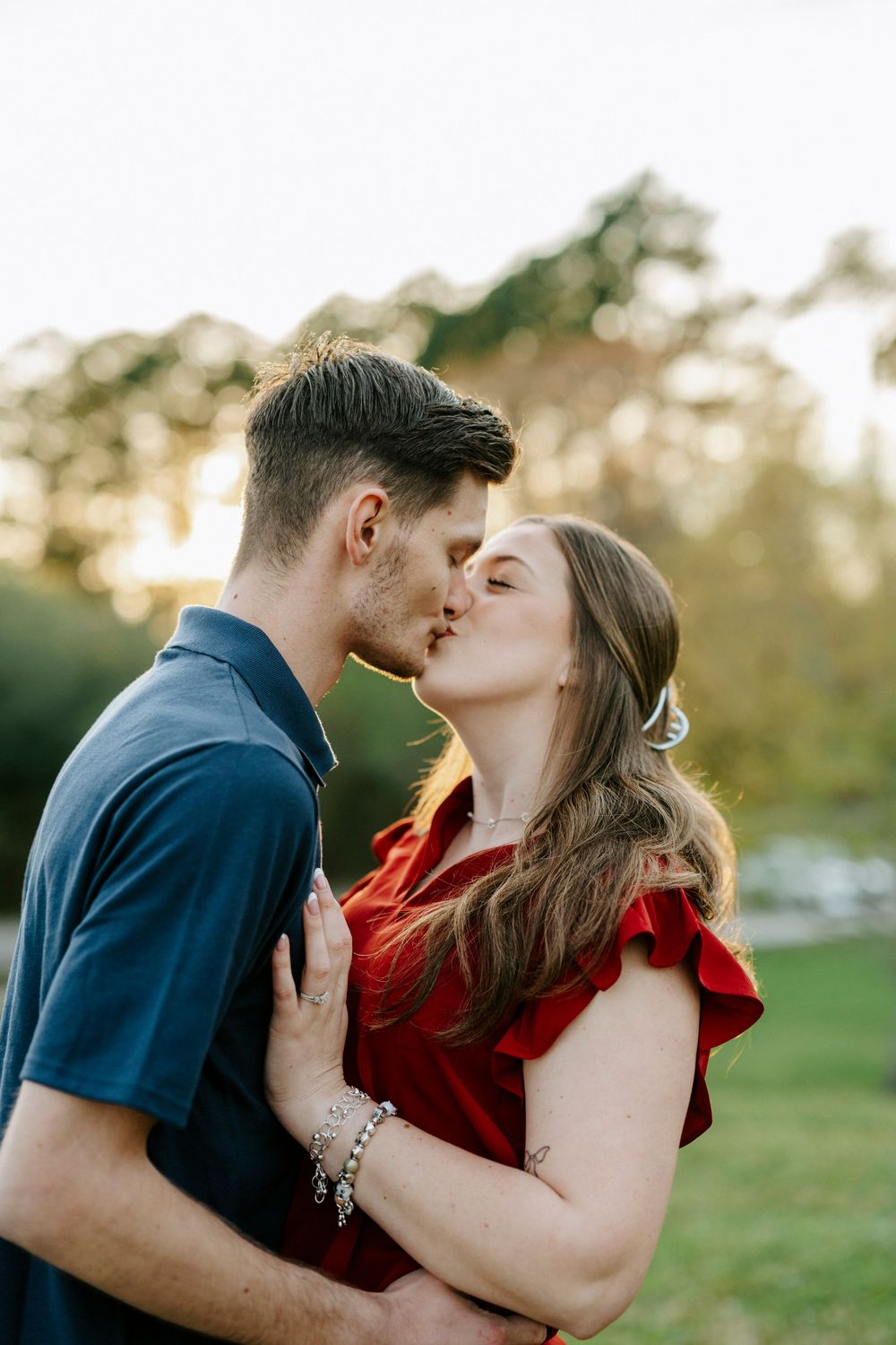 A couple shares a romantic kiss outdoors in a grassy field during golden hour.