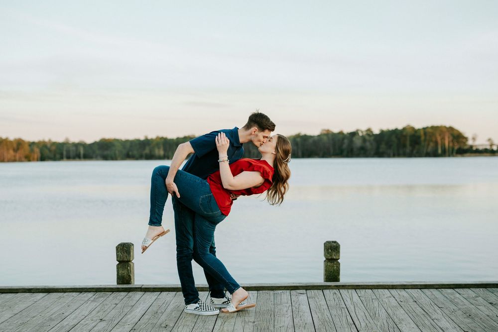A couple sits together on a wooden dock overlooking a serene lake during sunset.