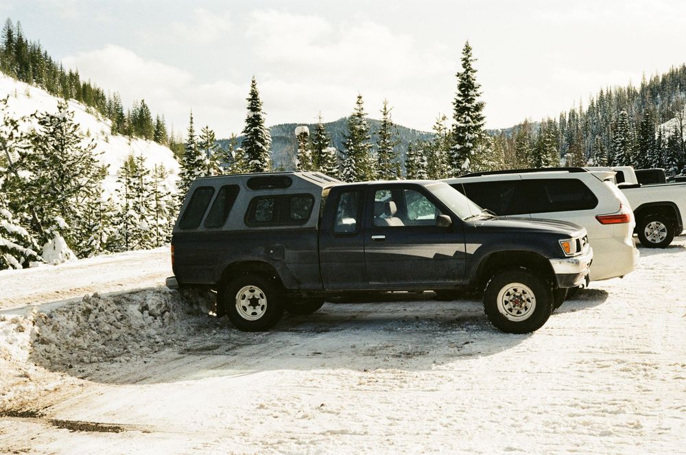 Dark blue SUV parked on a snowy mountain road surrounded by snow-covered evergreen trees in winter.