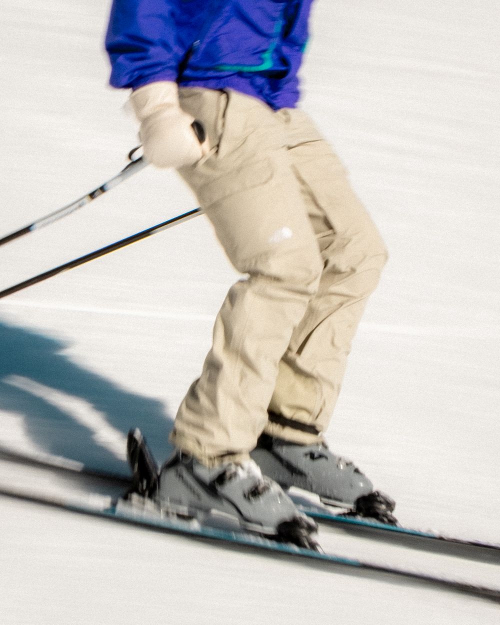 Motion blur sequence of a skier in blue and tan performing turns on a snowy slope.