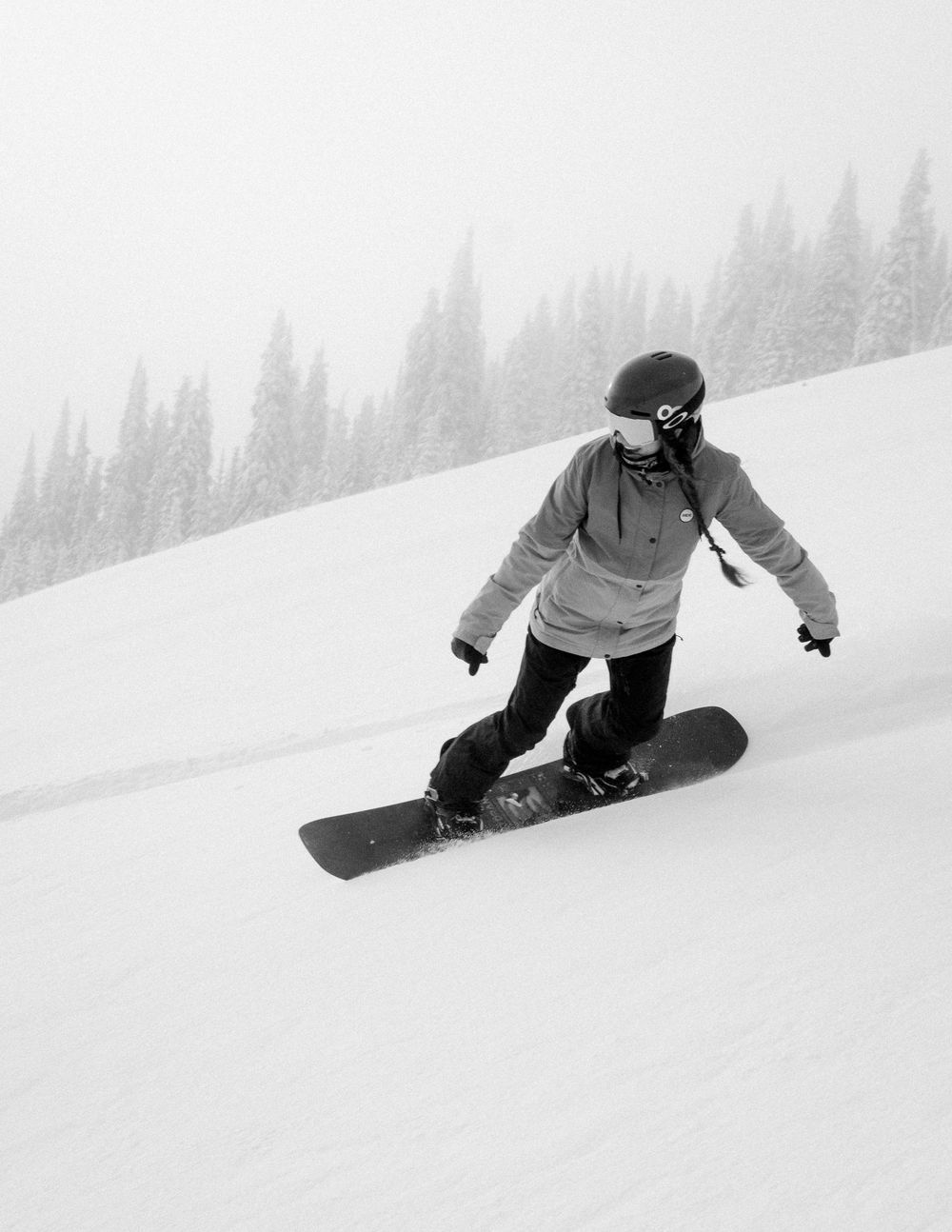 Snowboarder performing a low-angle turn on a pristine snow-covered slope in black and white.