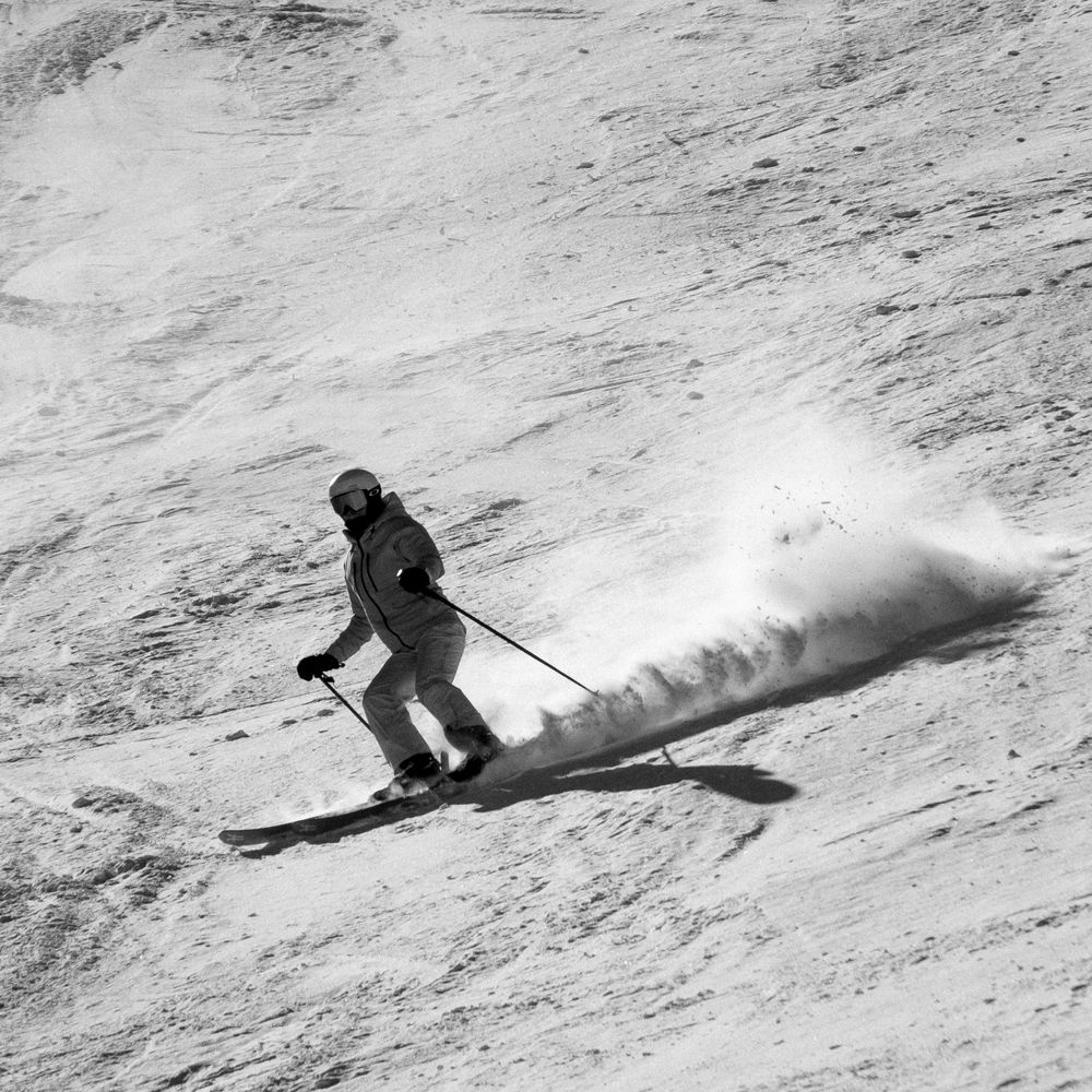 A skier carves through fresh powder snow creating dramatic trails of white spray while descending down a steep mountain slope.