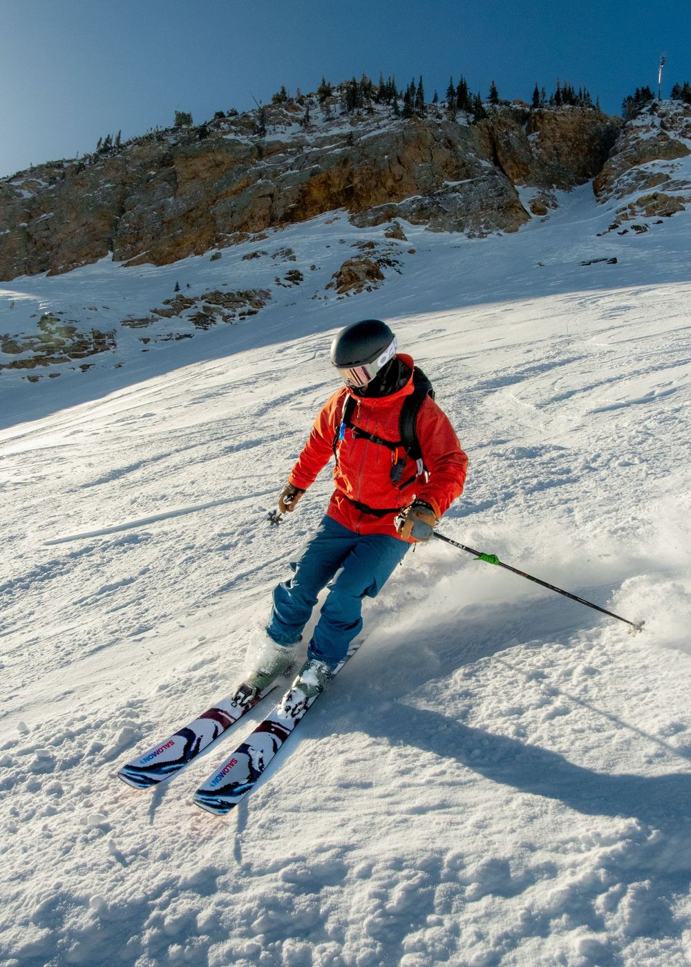 A skier carves through fresh powder snow on a steep mountain slope in a sequence of dynamic turning movements.