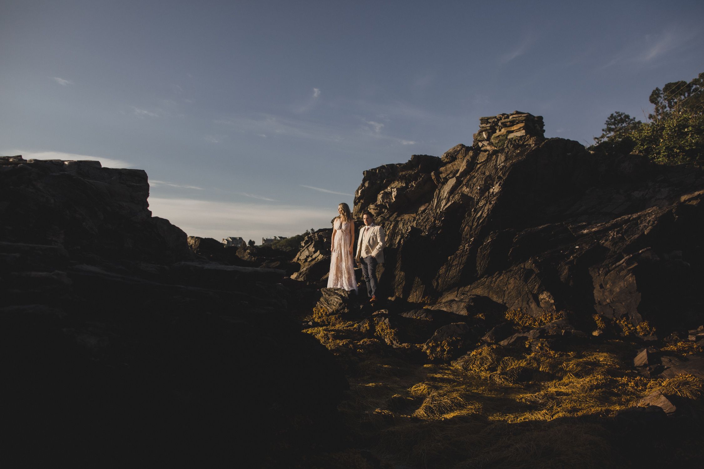 A couple explores rugged rocky terrain during golden hour with dramatic shadows and cliffs.