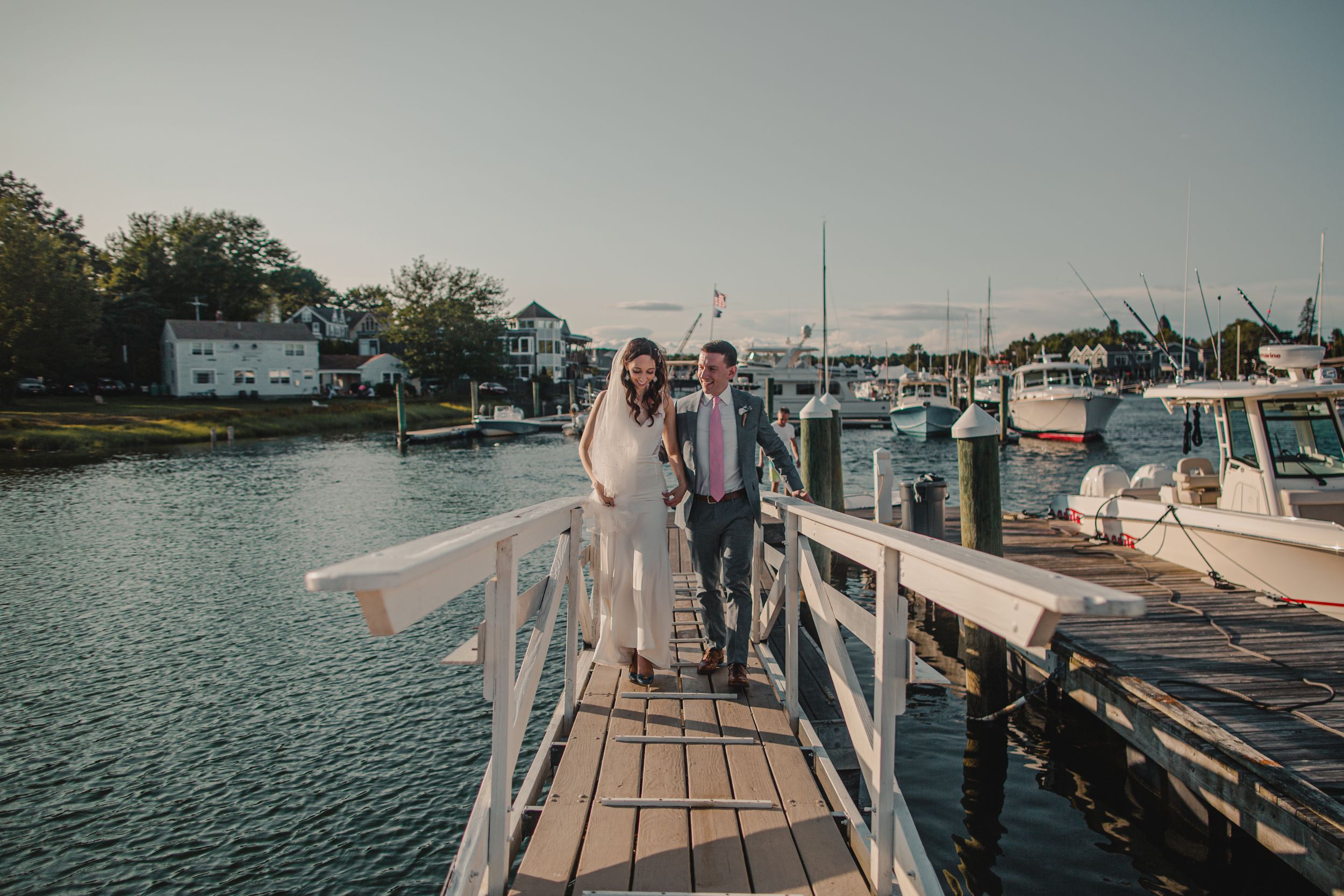 Scenic panoramic view of a wooden dock extending over calm waters with boats and buildings in the background.