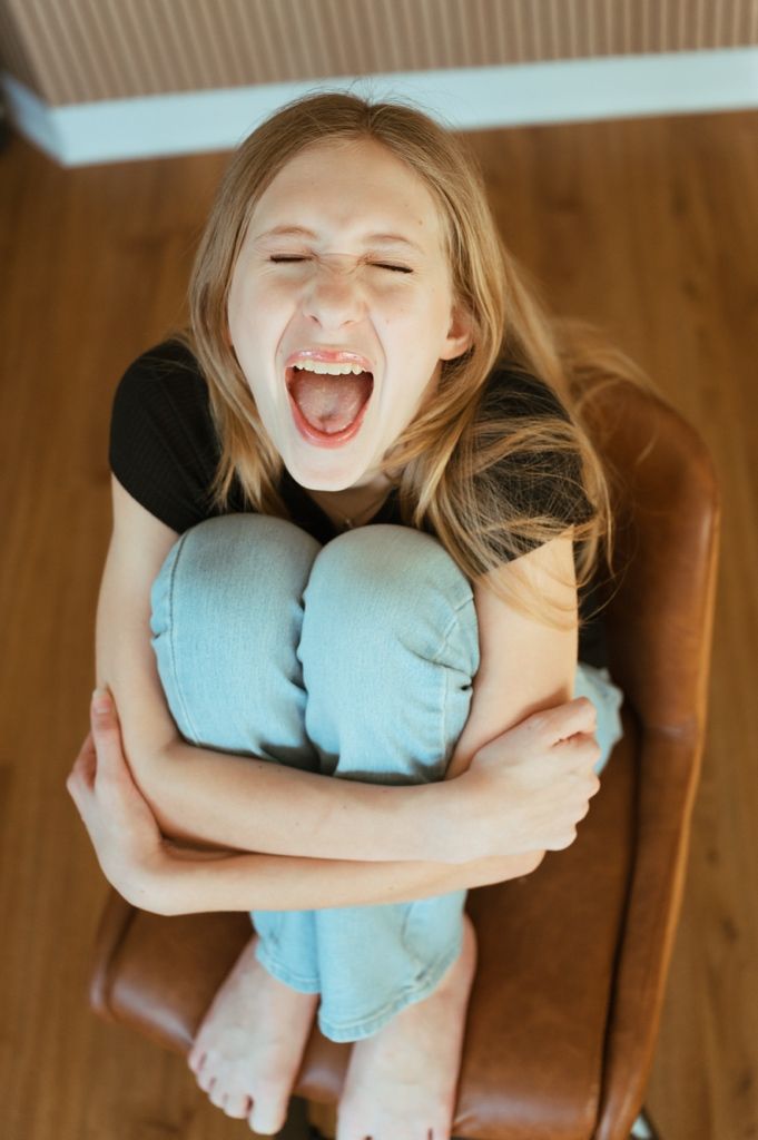 Candid sequence showing joyful expressions while hugging light blue pillow on leather furniture.