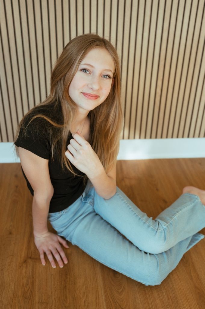 Young woman in black shirt lying on brown leather couch with light blue pillow showing playful expressions.