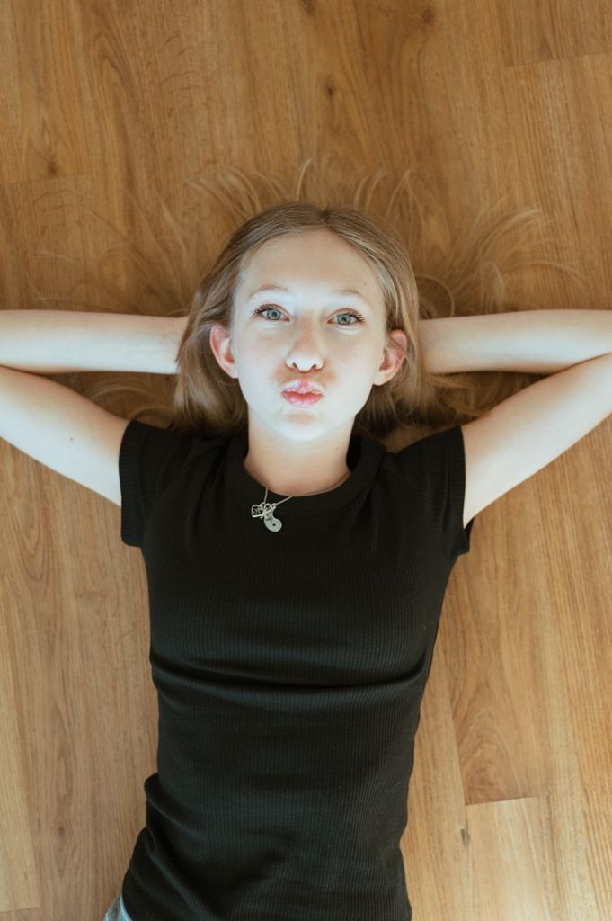 A sequence of playful expressions while lying on a wooden floor wearing a black top.