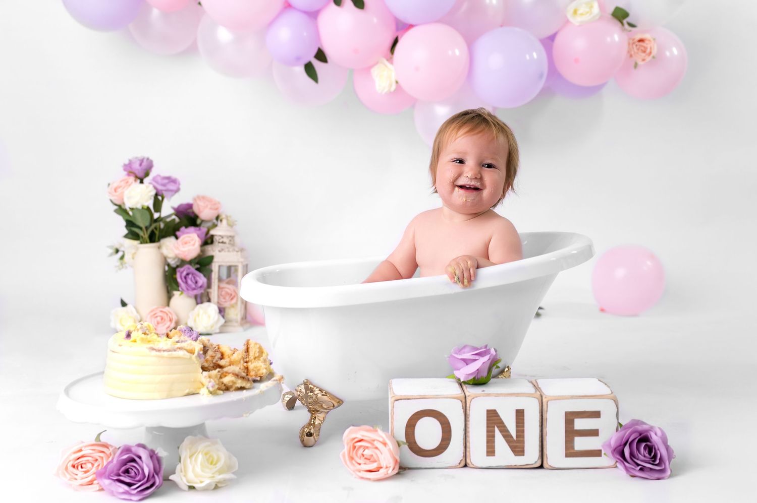 Smiling baby boy sitting next to wooden blocks spelling ONE, celebrating his first birthday milestone.