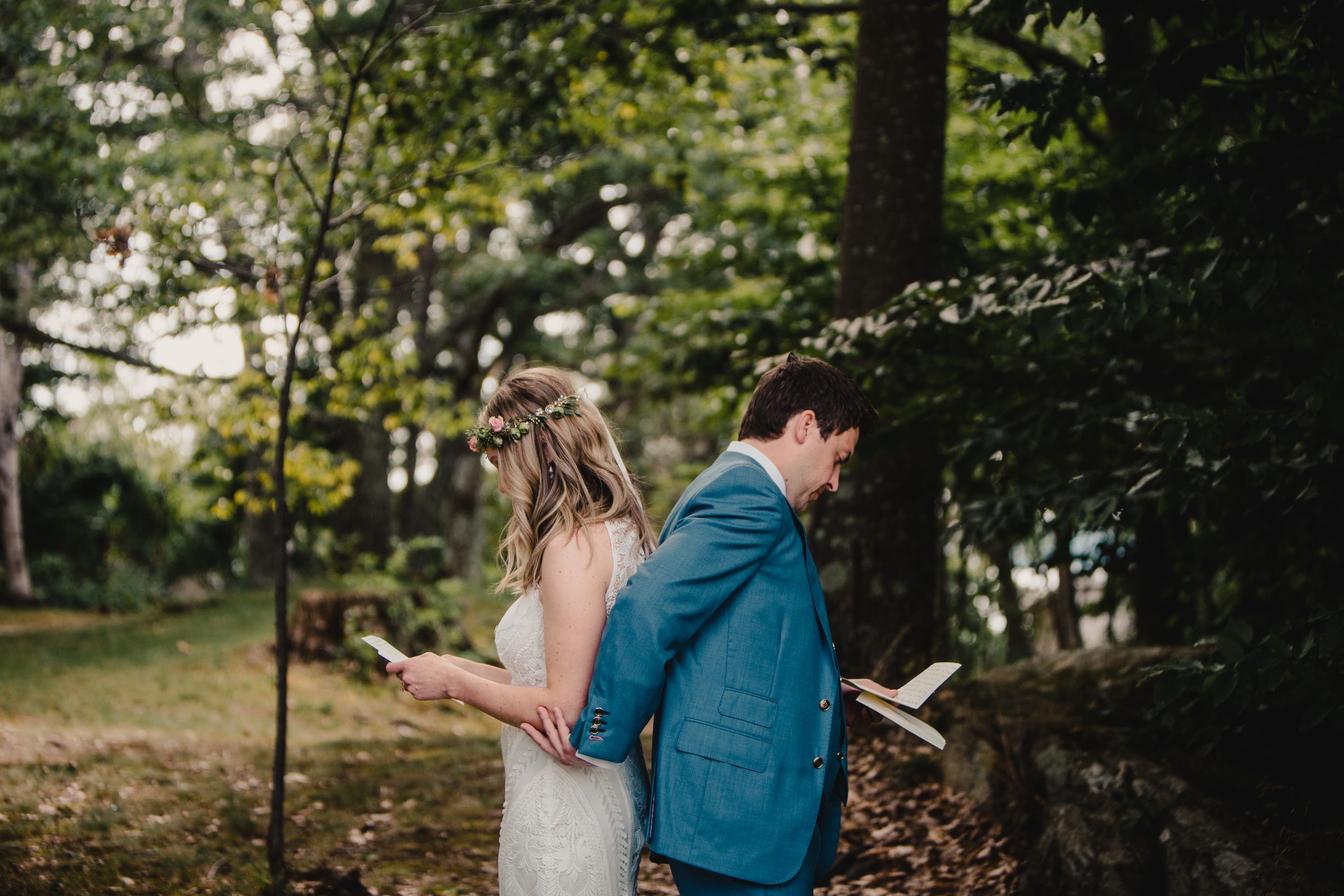 Bride and groom standing back-to-back reading personal vows in a lush green outdoor setting.
