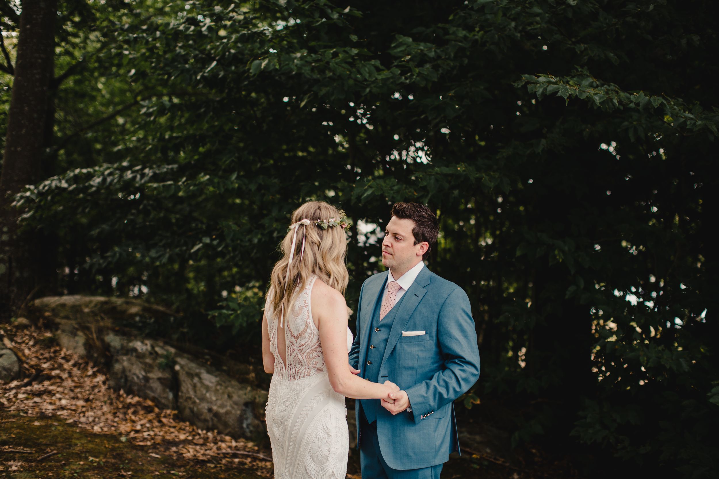 A bride and groom share a tender first look moment surrounded by lush green trees in an outdoor woodland wedding setting.